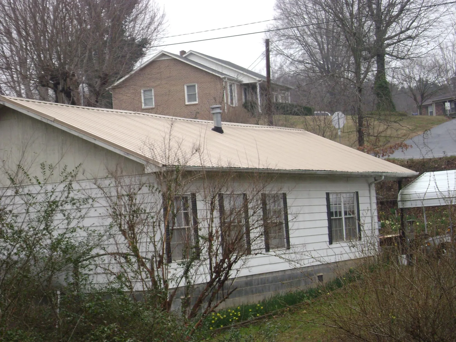 Tan metal roof on a white sided house set into a hillside — Commercial Roofing by Roofing Brothers in Hadley